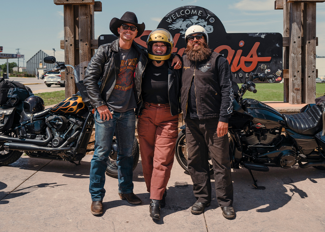 3 riders smiling in front of Sturgis sign