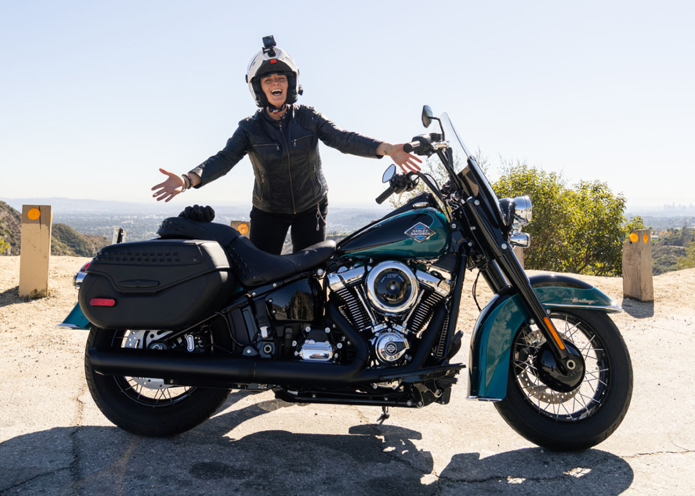 A person standing behind a teal HD motorcycle at a scenic overlook
