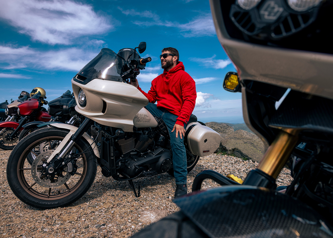 A rider wearing a red jacket sitting on a touring motorcycle at a mountain overlook